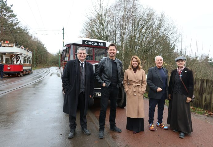 Five figures stood in front of vintage bus.