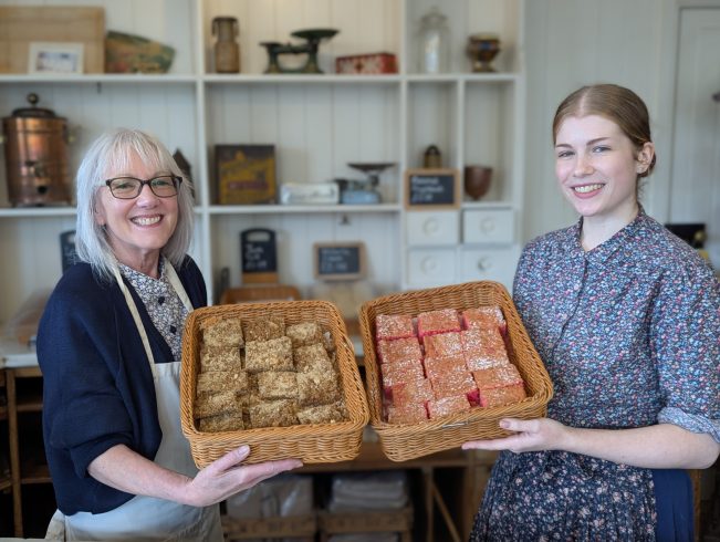 Two members of staff holding selection of baked goods inside Heron's Bakery.