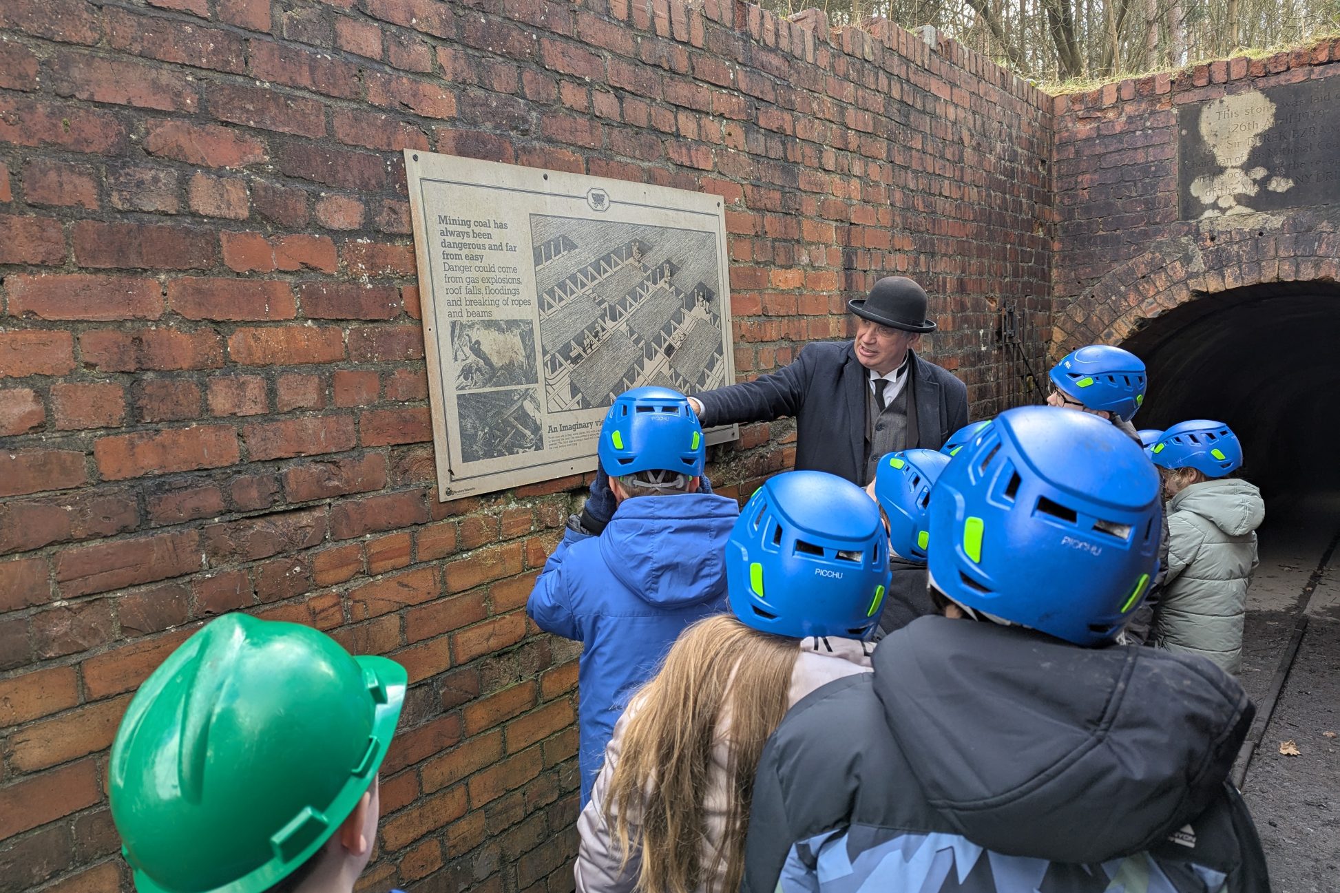 Group of young people wearing hard hats, with staff member looking at poster on the wall.