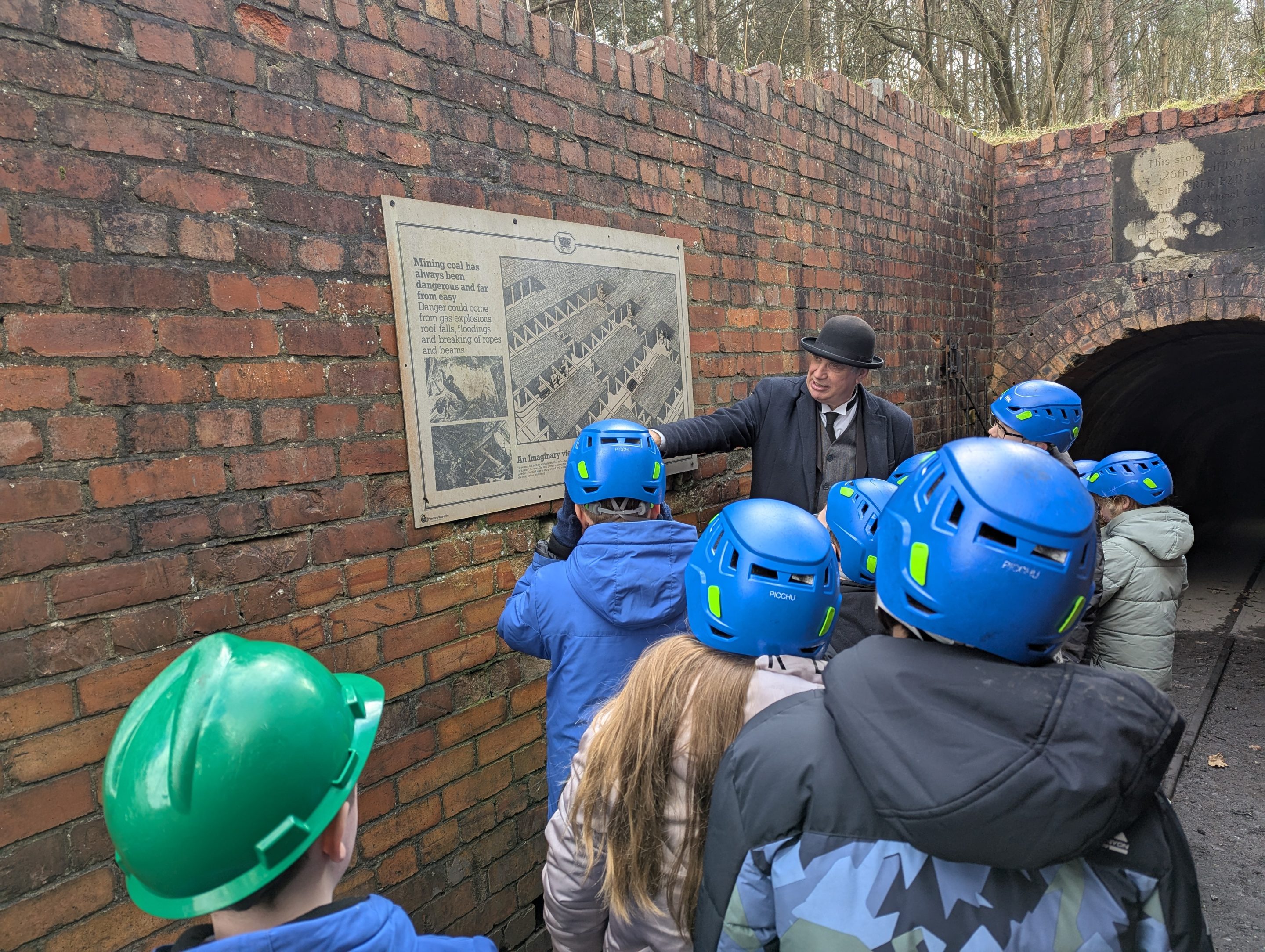 Group of young people wearing hard hats, with staff member looking at poster on the wall.