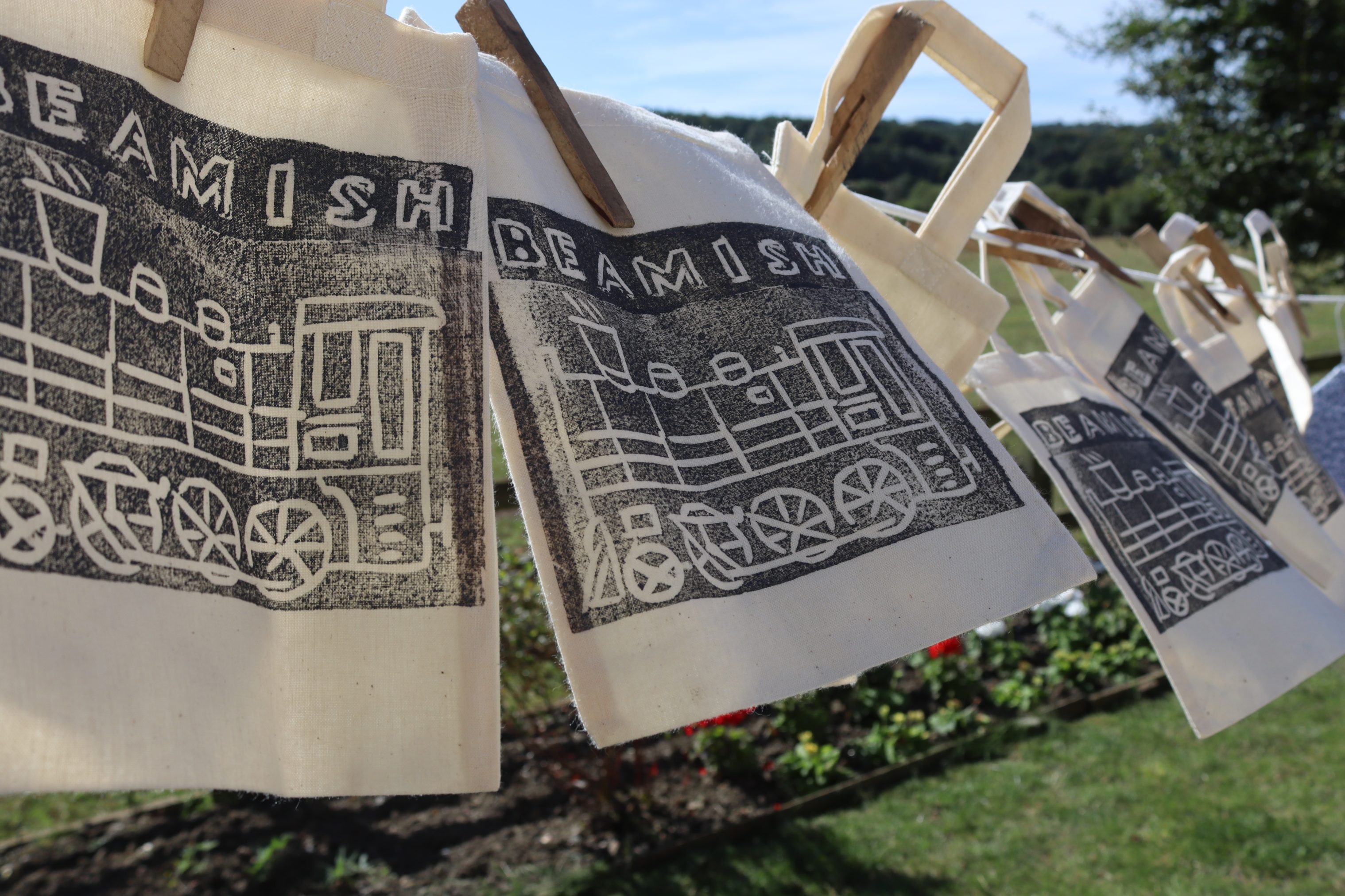 Printed tote bags drying on a washing line.
