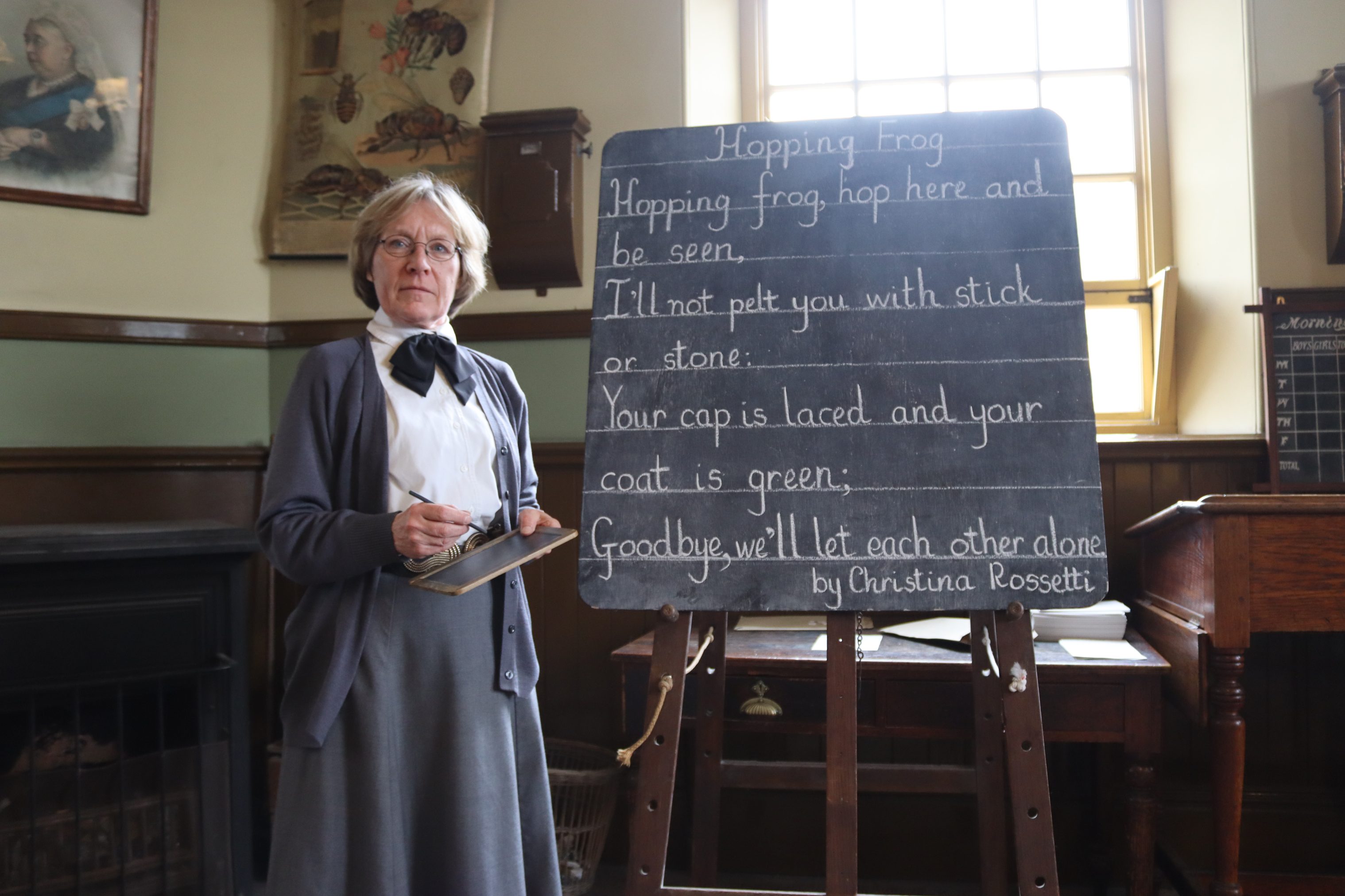 Costumed staff member next to blackboard in 1900s Pit Village school.