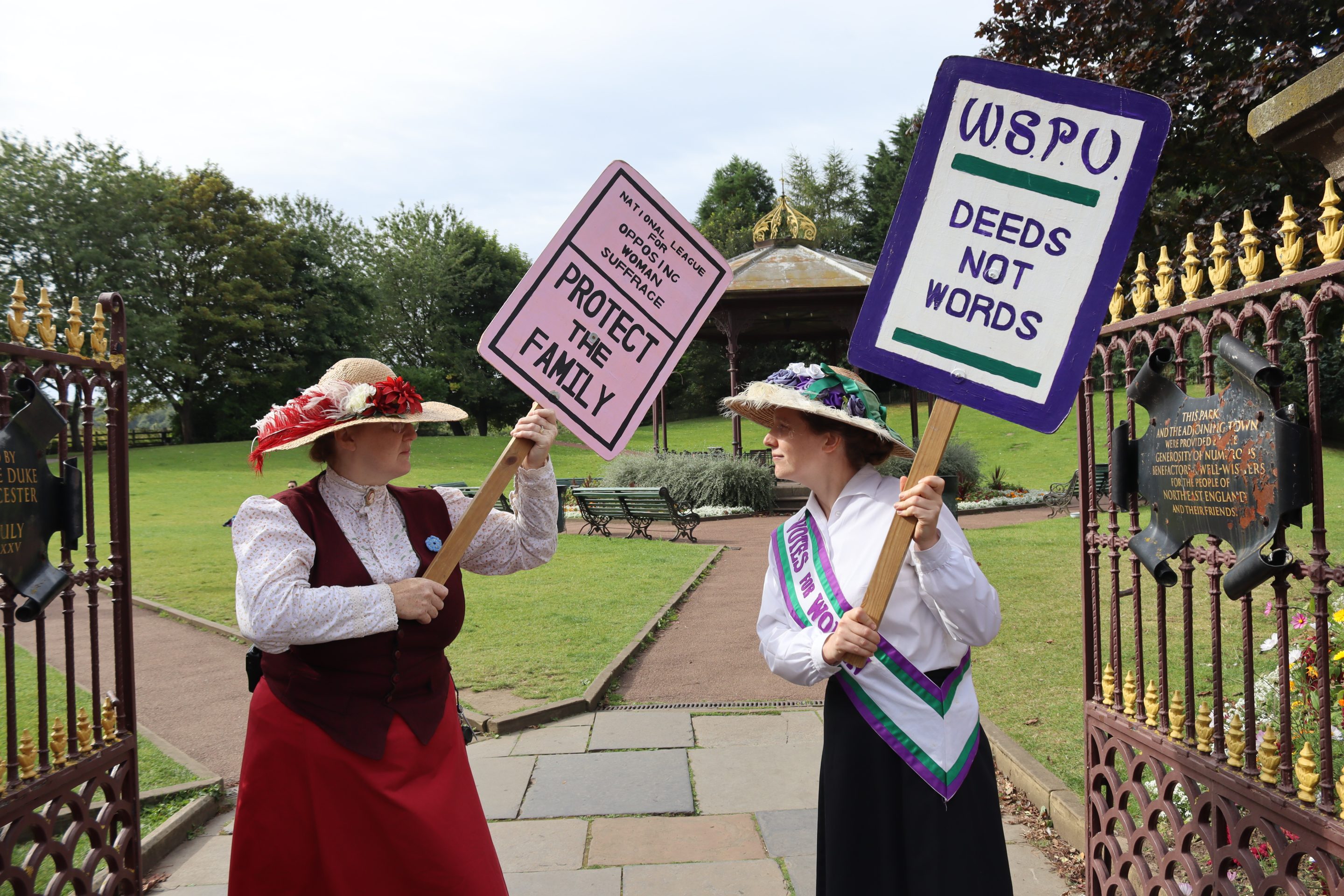 Two staff members dressed in Edwardian costume, with messages opposing and for women's suffrage.