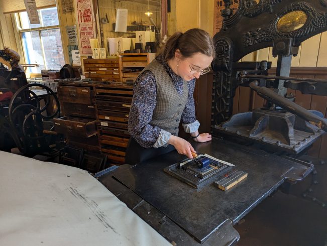 Costumed staff member rolling ink onto print block.