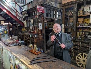 Costumed staff member in garage holding tool.