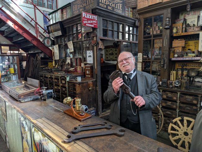 Costumed staff member in garage holding tool.