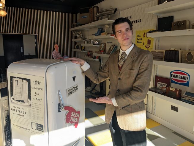Figure pointing towards vintage fridge.