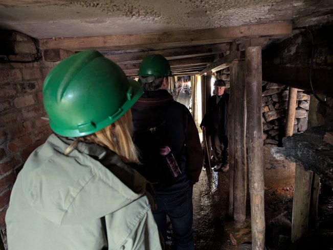 Staff member leading visitors wearing hard hats through drift mine.