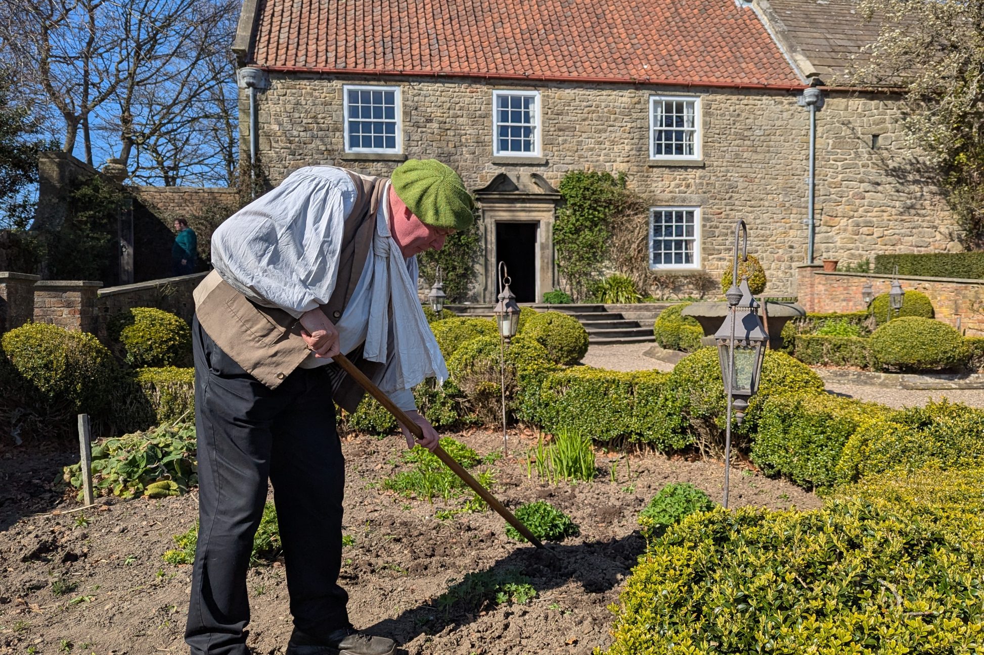 Figure gardening in front of large house.