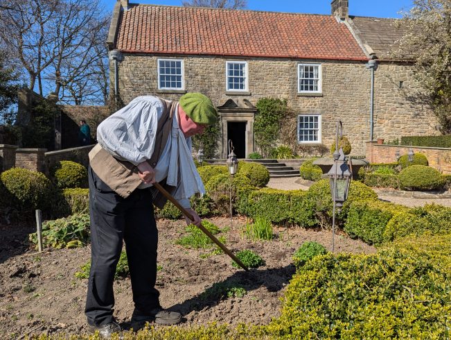 Figure gardening in front of large house.