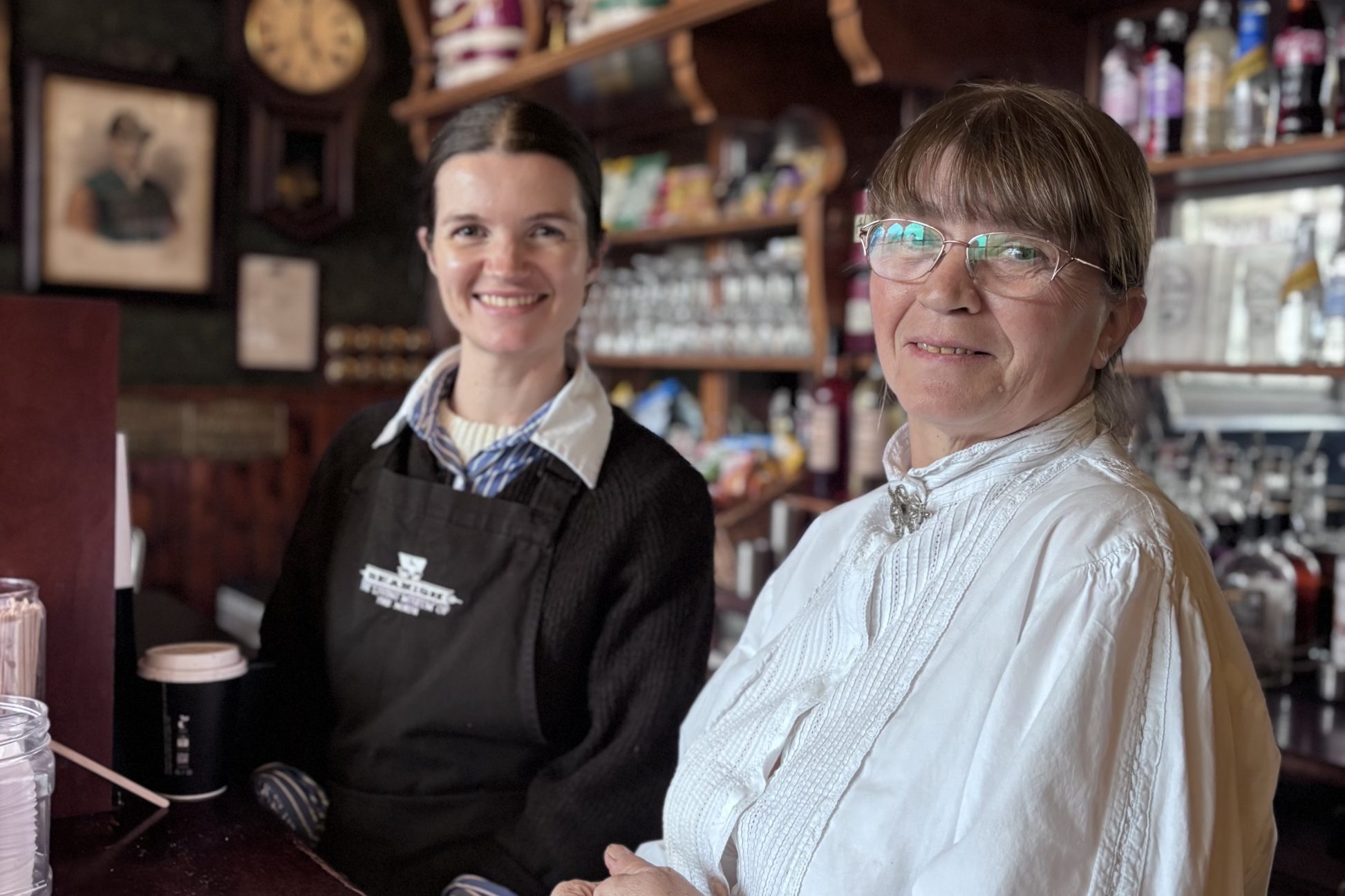 Two costumed staff members behind pub bar.