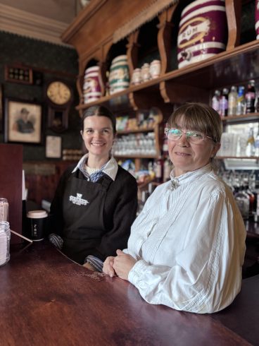 Two costumed staff members behind pub bar.