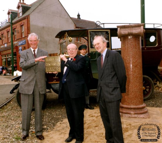 Figures in suits holding Barclays Bank sign.