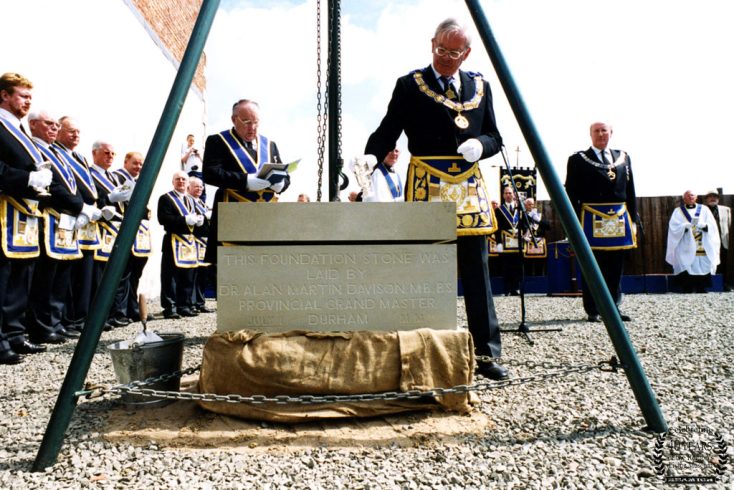 Main figure wearing chain laying foundation stone, surrounded by others.