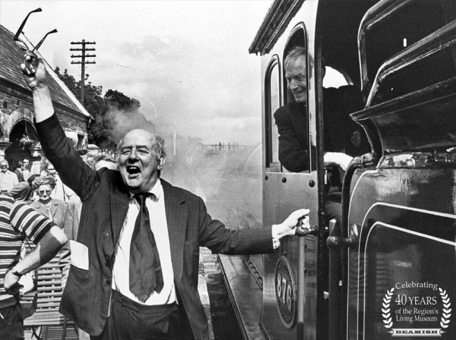 Figure with arm waved in the air, stood next to steam train.