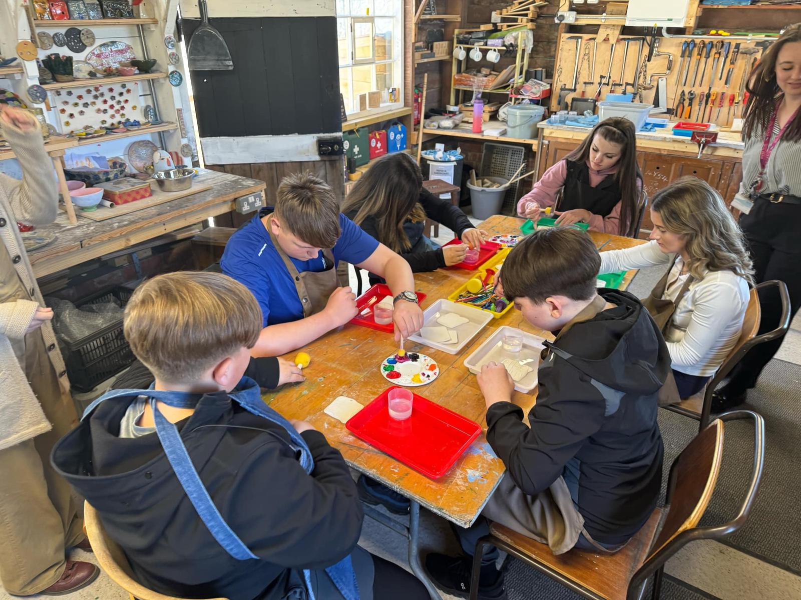 A group of young people sit around a table painting.