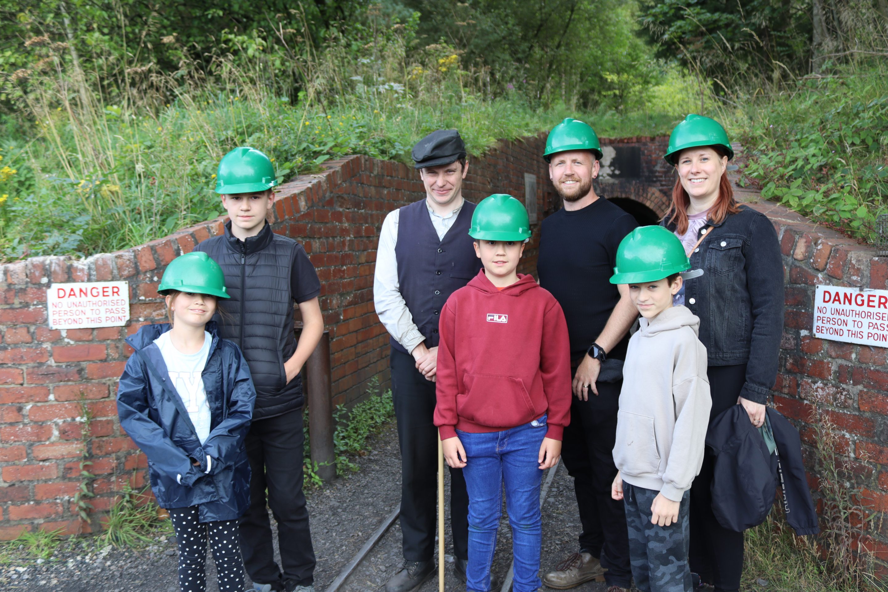 Family wearing hard hats at colliery mine entrance.
