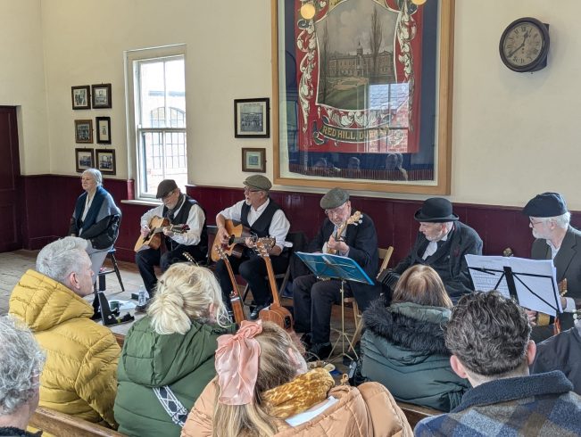 Band members with instruments playing to a crowd of people.