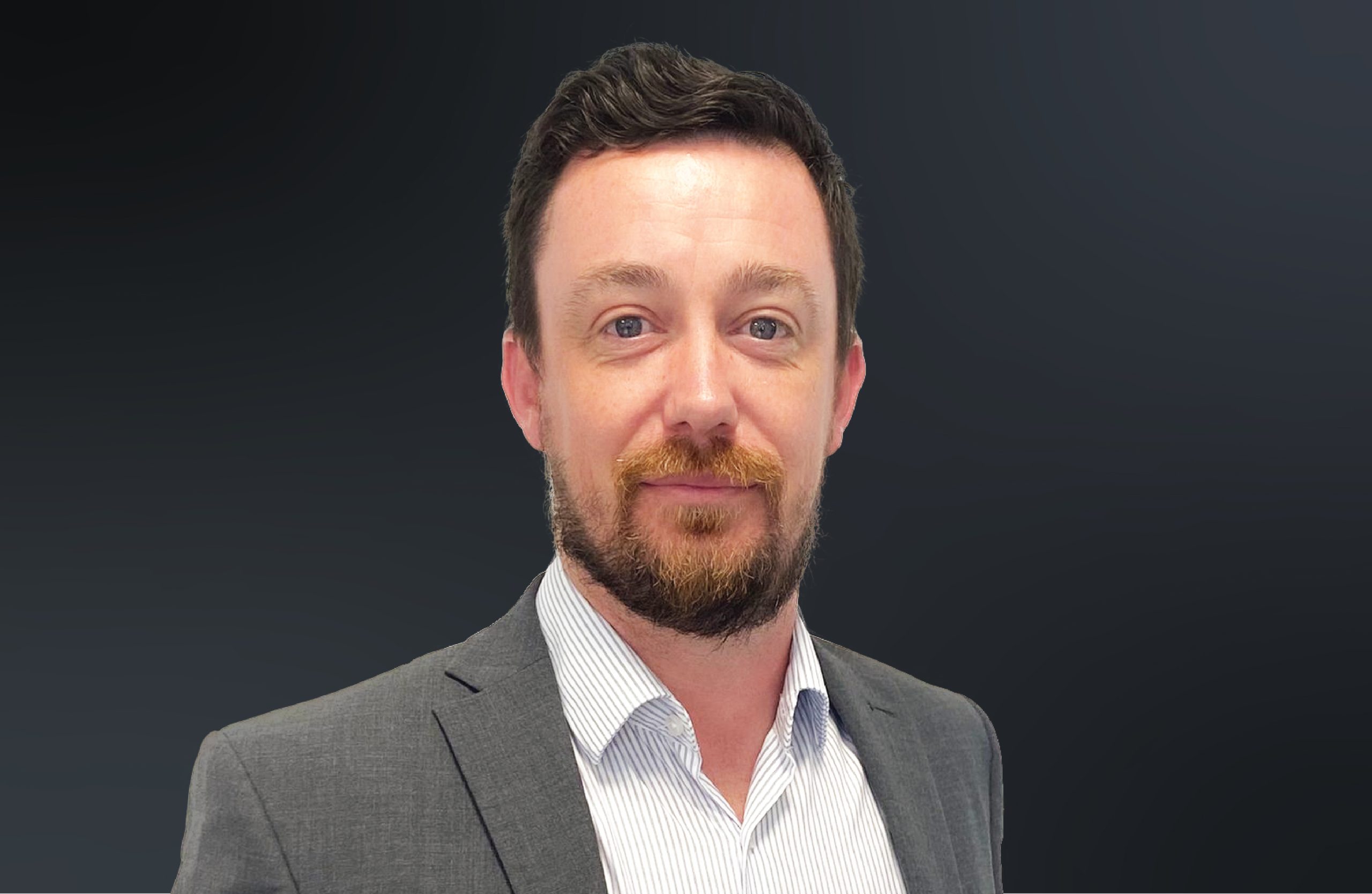 A head shot of Michael Cox wearing a grey suit against a dark background