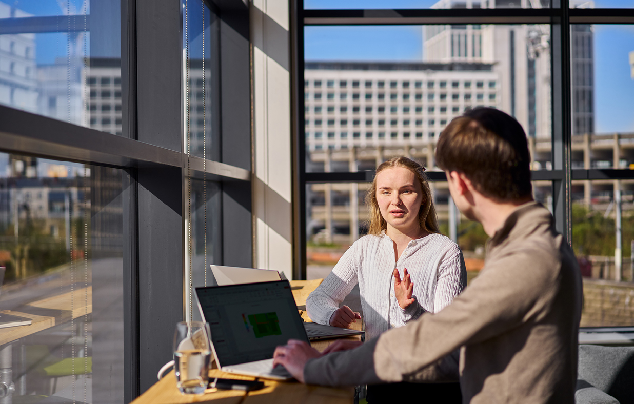 Cat and another male graduate having a meeting next to windows over looking a cityscape in the background.