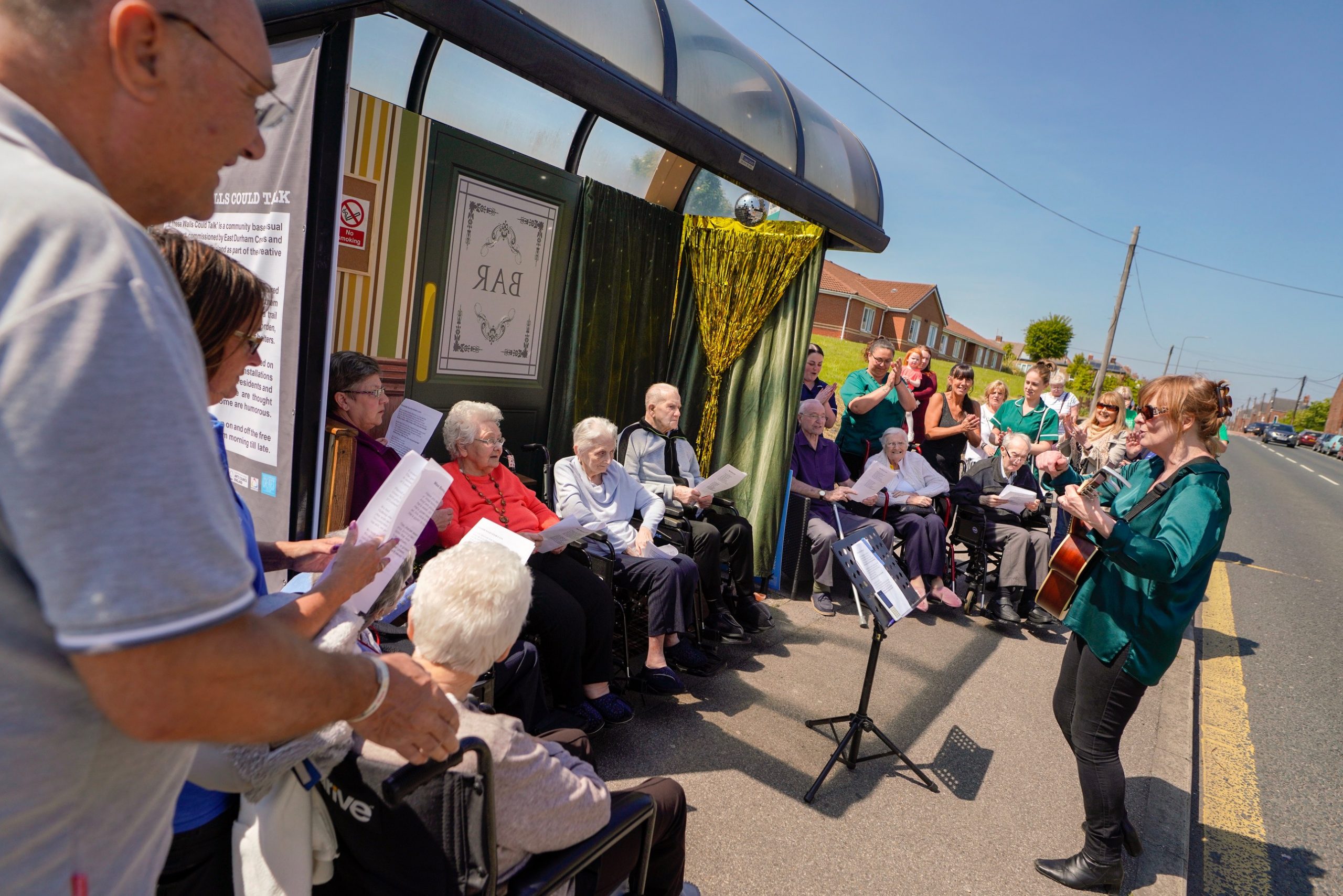 Care home residents being entertained by a singer in a bus shelter as part of an East Durham creates project