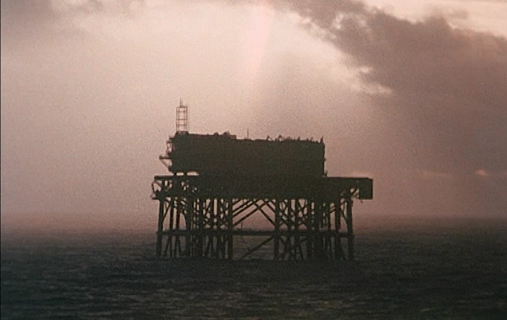 An oil rig is silhouetted against a sepia coloured sky.