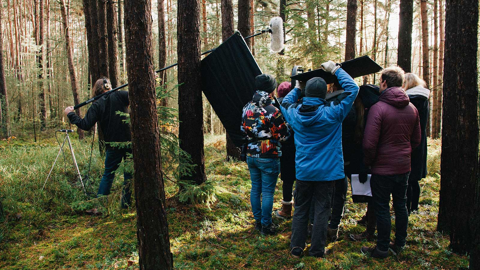 A group of people stand outside filming in a forest.