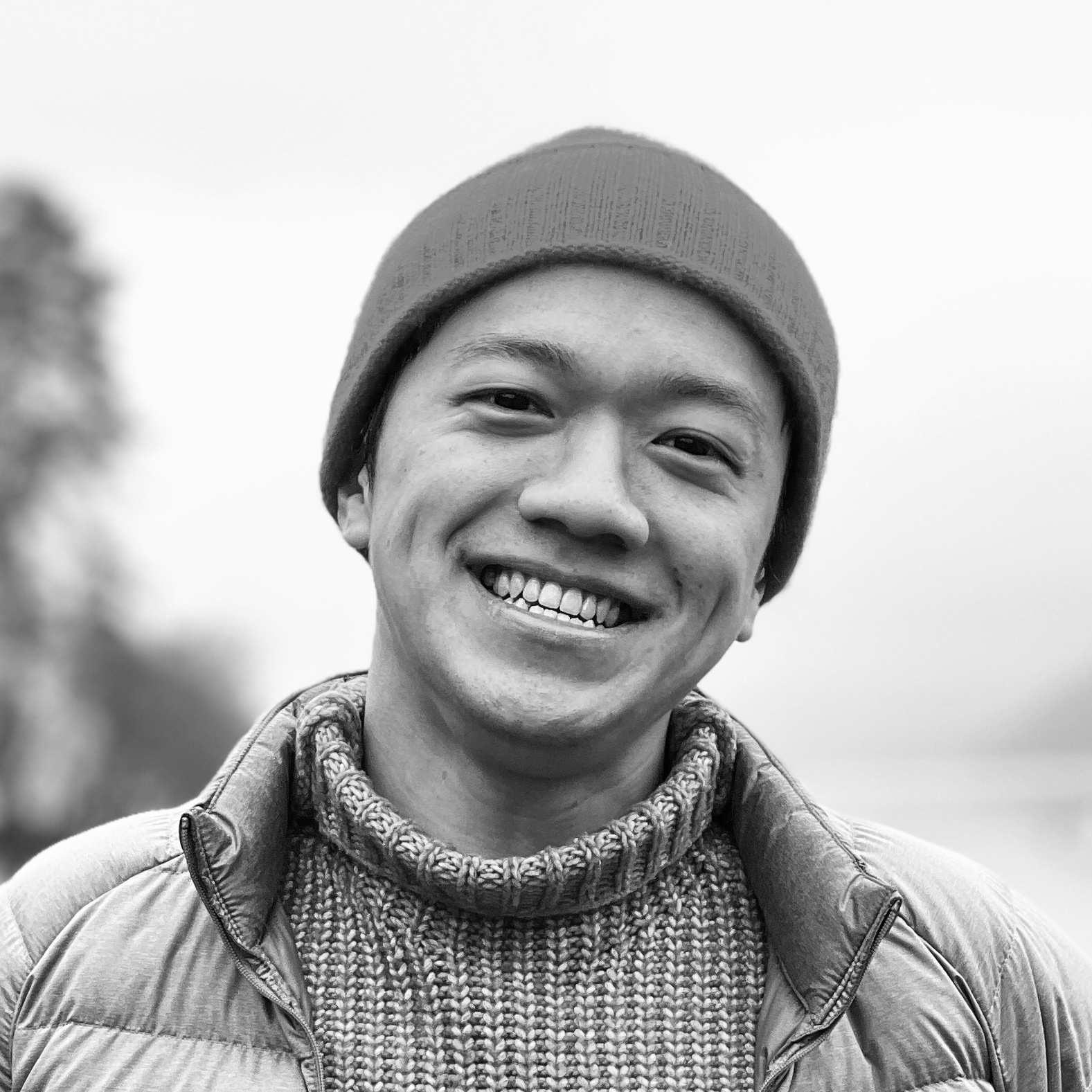 Black-and-white photo of Chak, a young Cantonese man smiling and wearing a turtleneck knitted sweater and a beanie