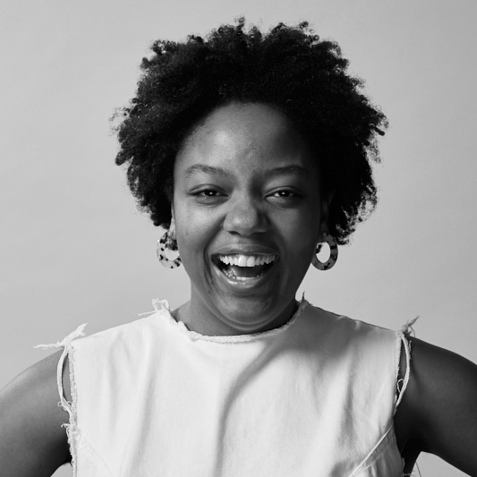 Black-and-white headshot of Briana Pegado smiling and laughing at the camera, with short natural hair and wearing a light sleeveless top.