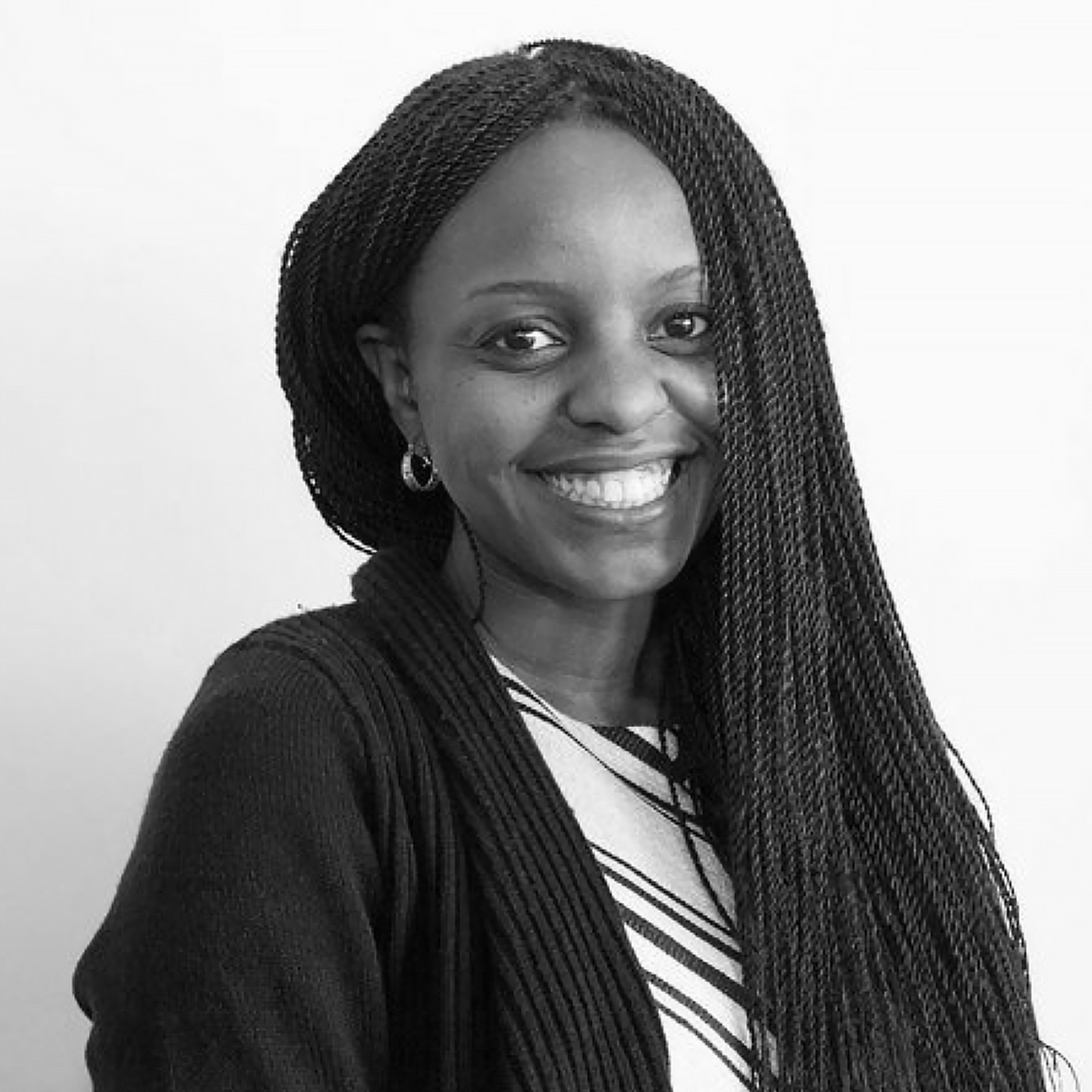 Black-and-white headshot of Liz Chege smiling at the camera, with long braided hair and wearing a dark cardigan over a patterned top.