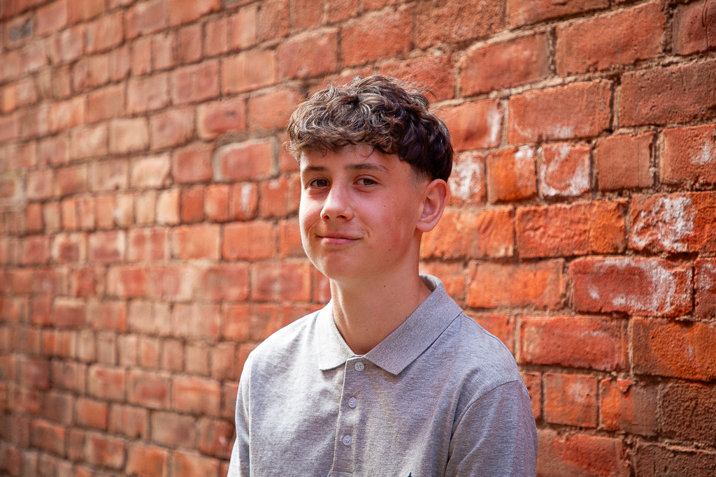 A young boy against a brick wall.