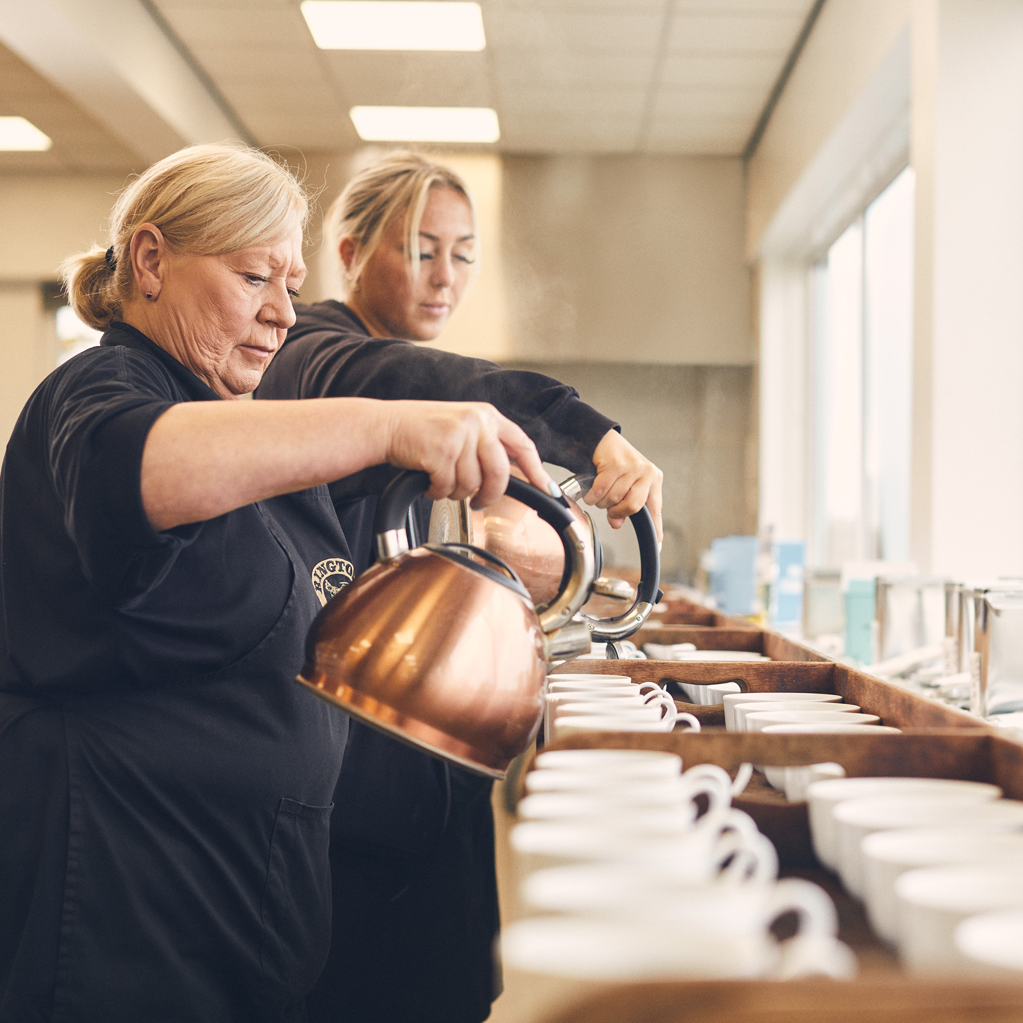 Two people holding kettles pouring liquid into cups.