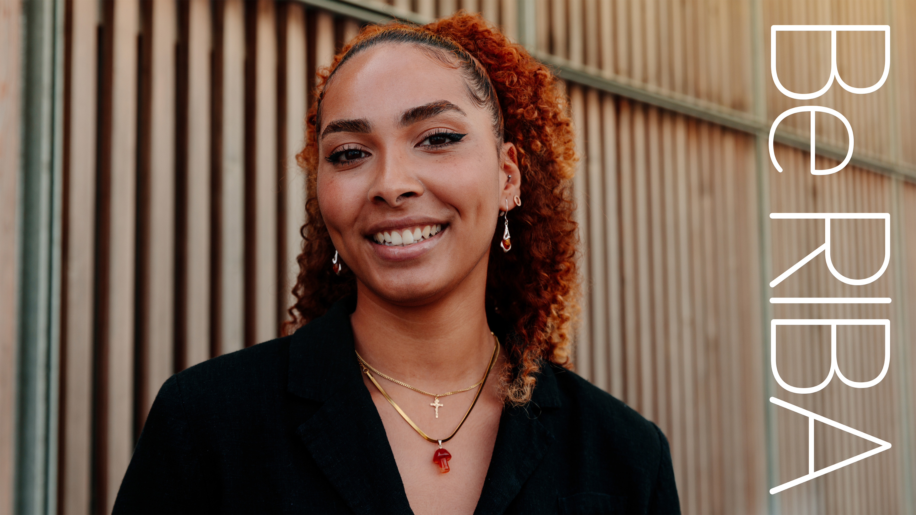 Smiling person with orange hair against wooden backdrop.