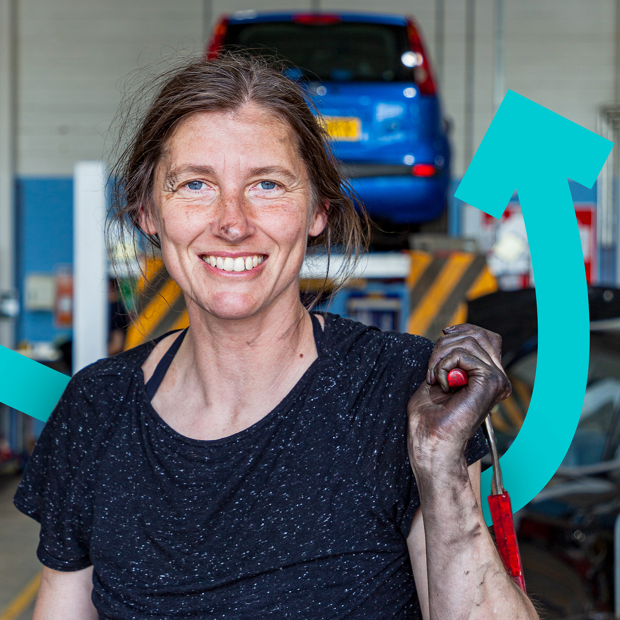Person smiling with dirty hands holding tool in front of car.