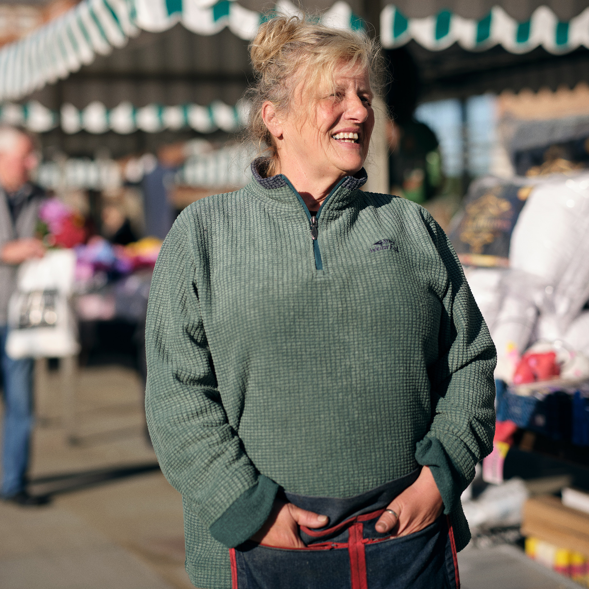 North East person with long hair wearing a green jumper and smiling.