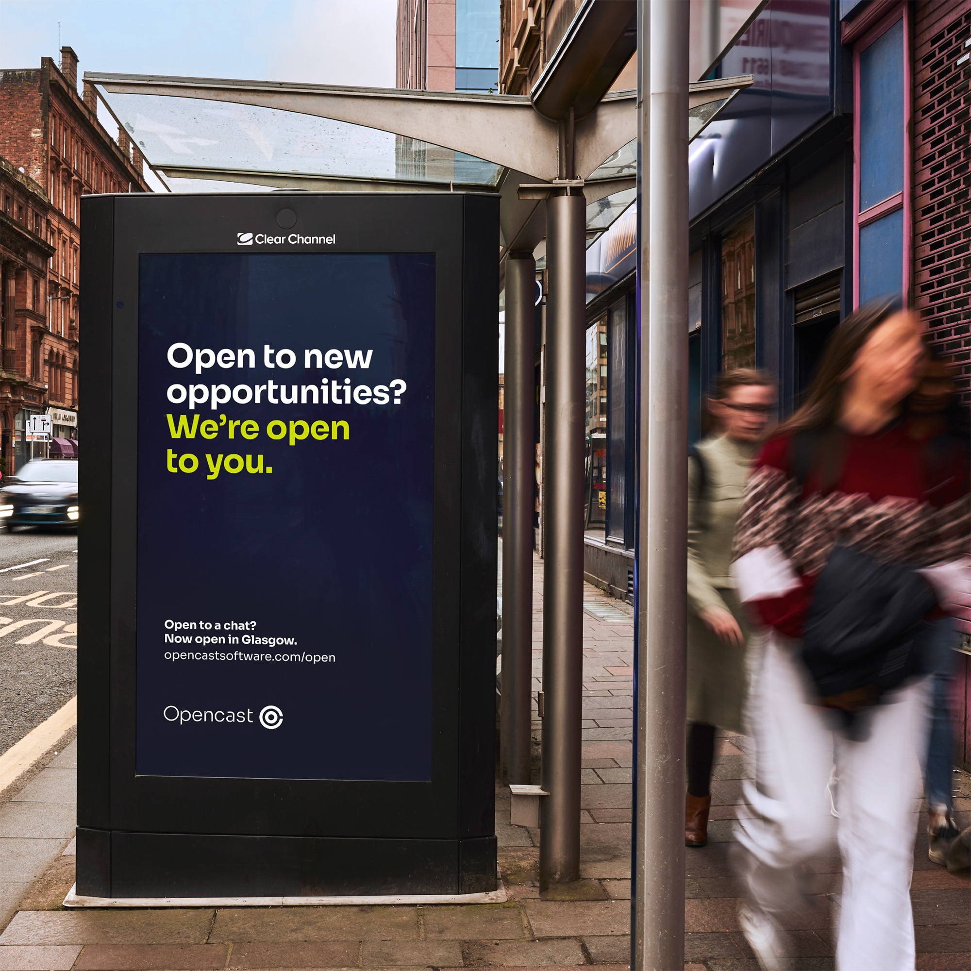 Bus stop shelter with Opencast advertising as people walk past on a busy street.