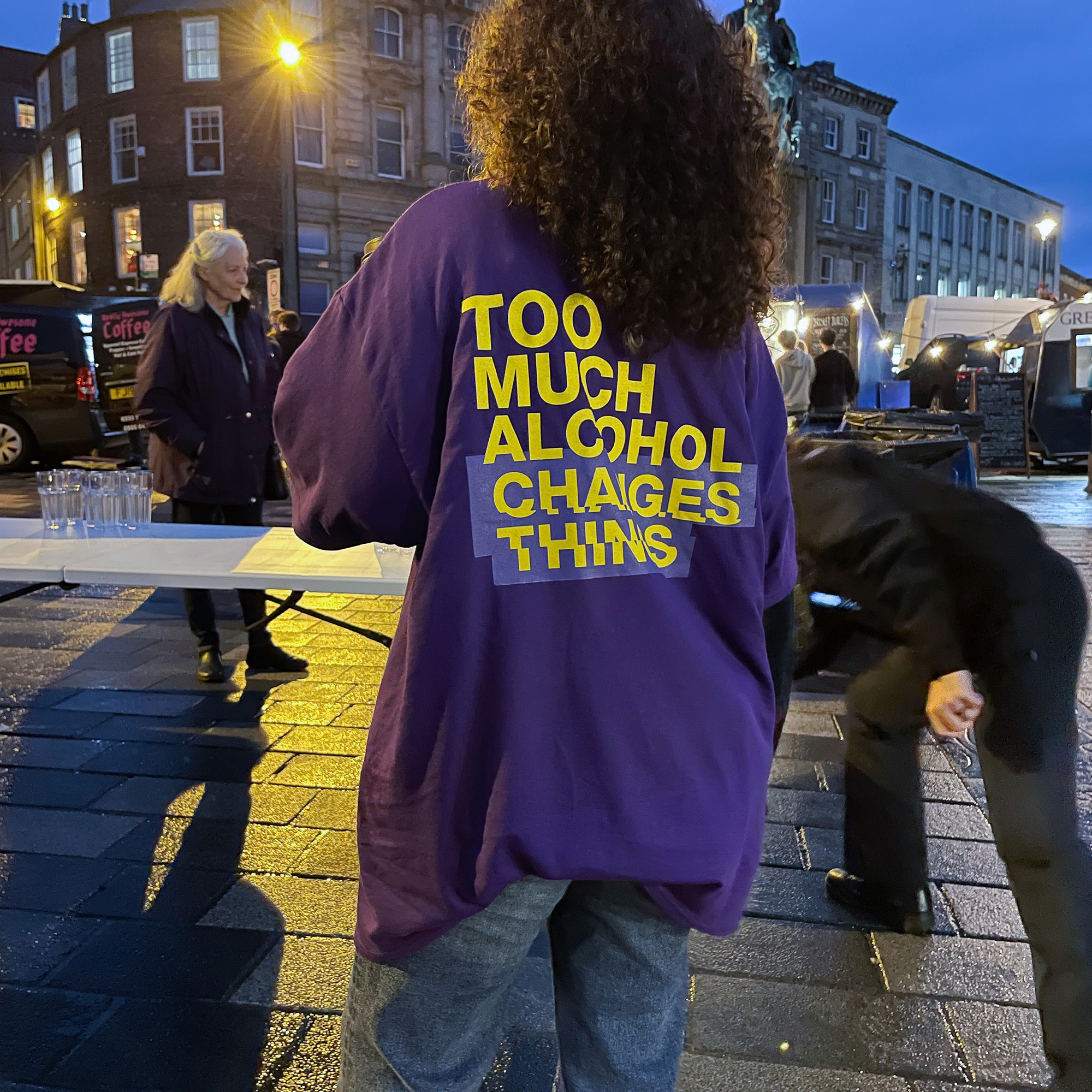A woman wearing a purple t-shirt faces other people near Monument, Newcastle.