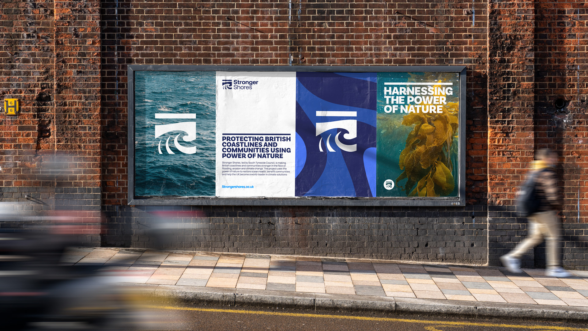 Someone walking past four posters against a brick wall