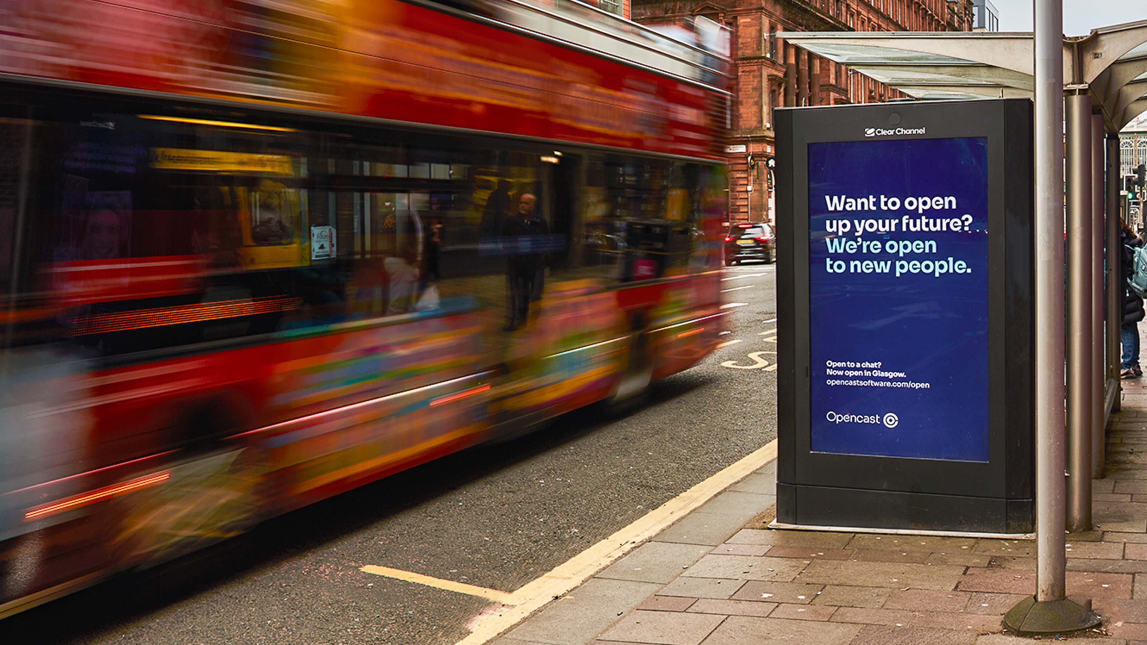 Red bus passing a bus stop in Glasgow city centre showing advert for Opencast software