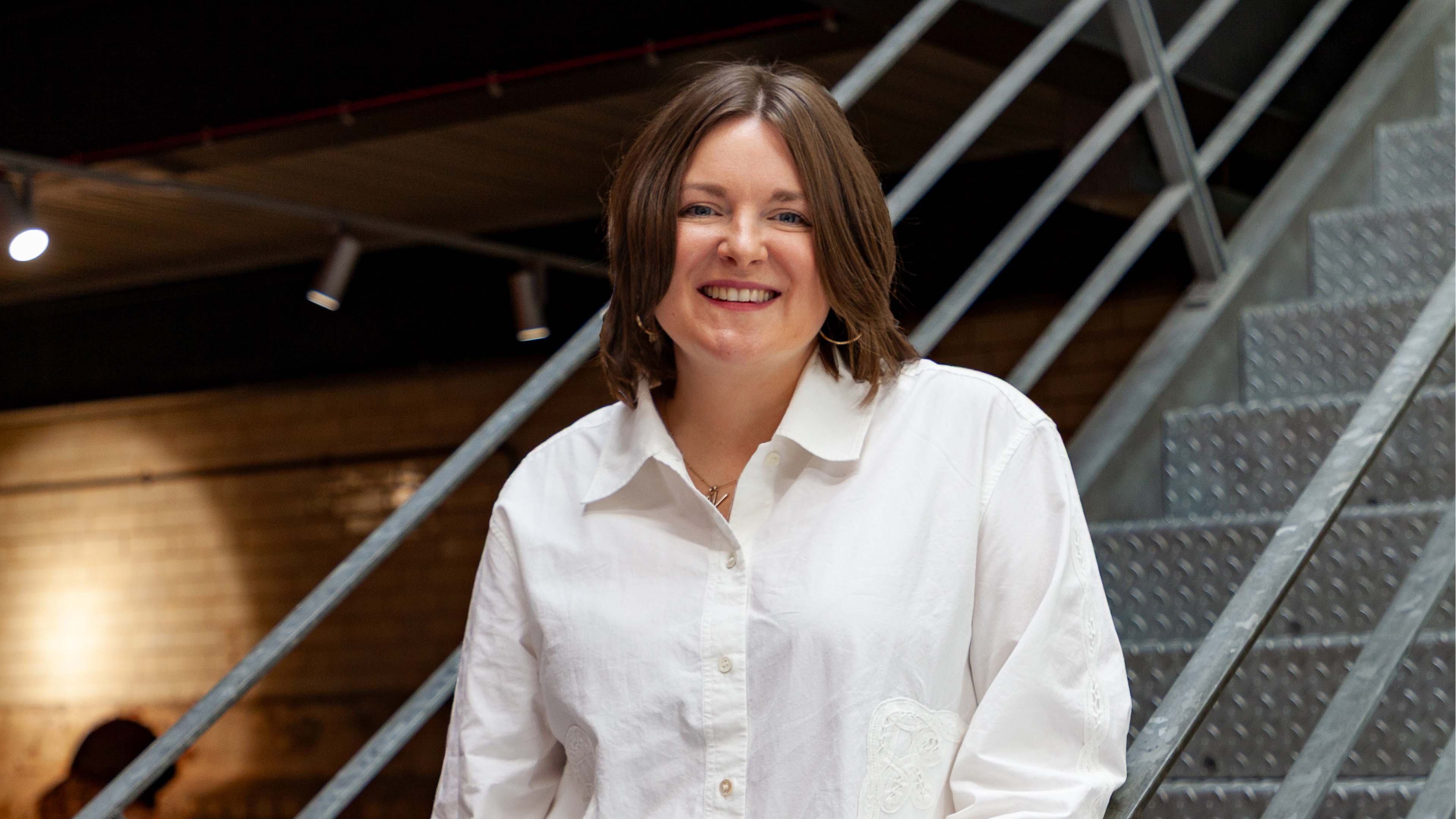 Jen smiling in front of a metal staircase inside an office