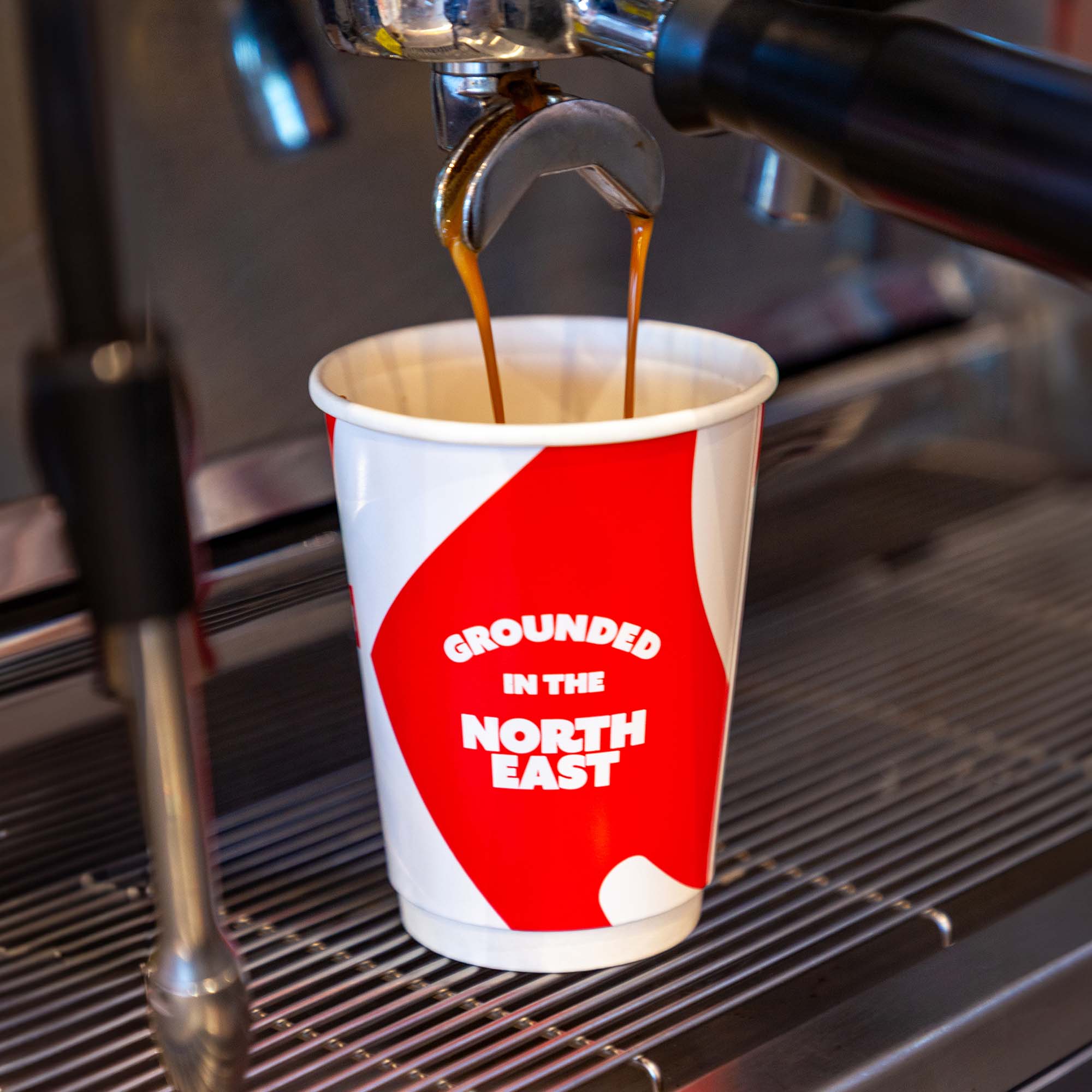Fresh coffee being poured into a newly brand Dicksons takeaway cup. The cup has the wording Grounded in the North East to capture the family's playful character