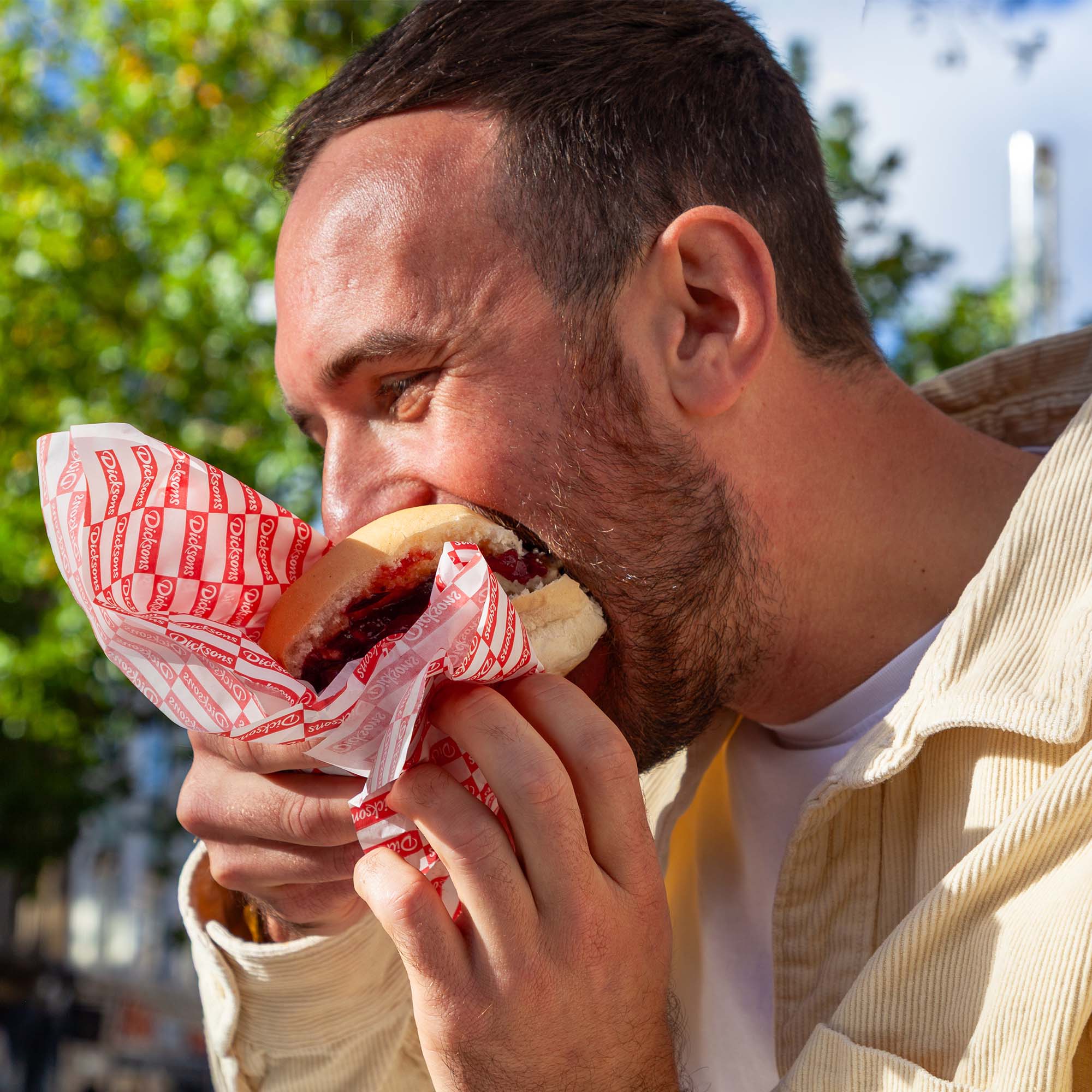 Young male eating a deep filled Dicksons sandwich on a sunny day in central Newcastle. The sandwich is held in the a branded Dicksons sandwich wrapper.