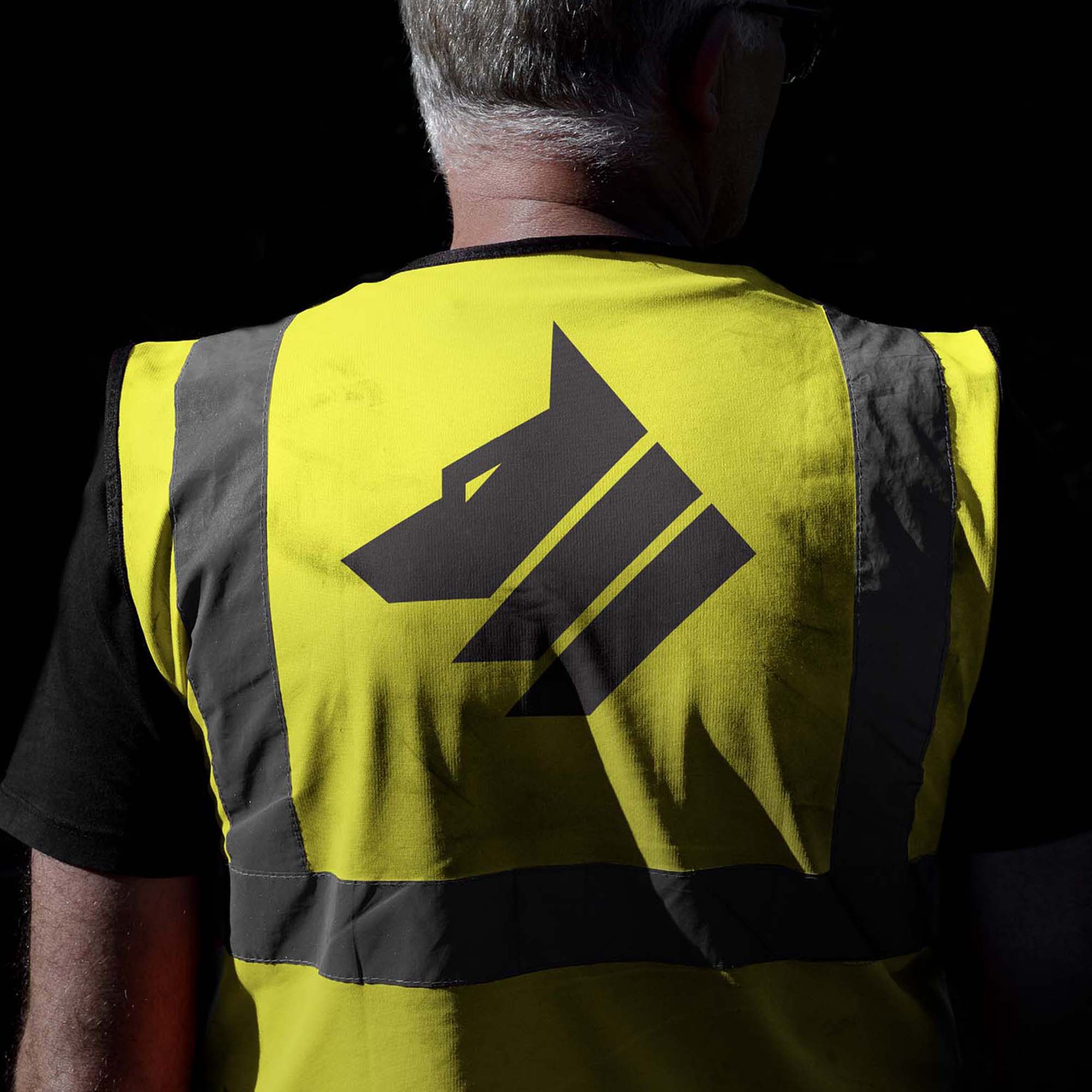 Back of workman wearing a high visibility vest with the Universal Wolf logo printed on it in black against a black background
