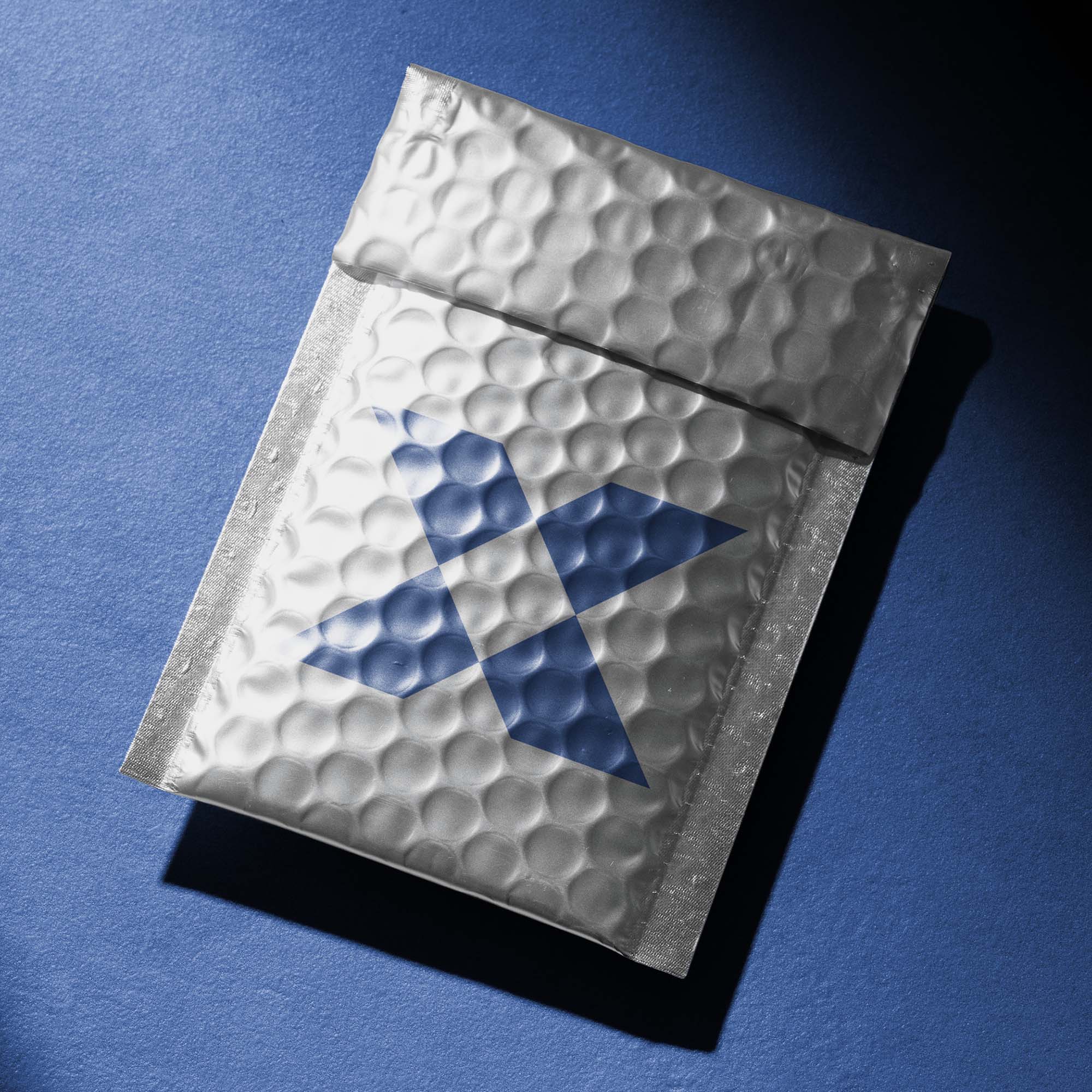 Tioxed X symbol printed on the back of a silver padded envelop which is laying on a blue background the same colour as the X.