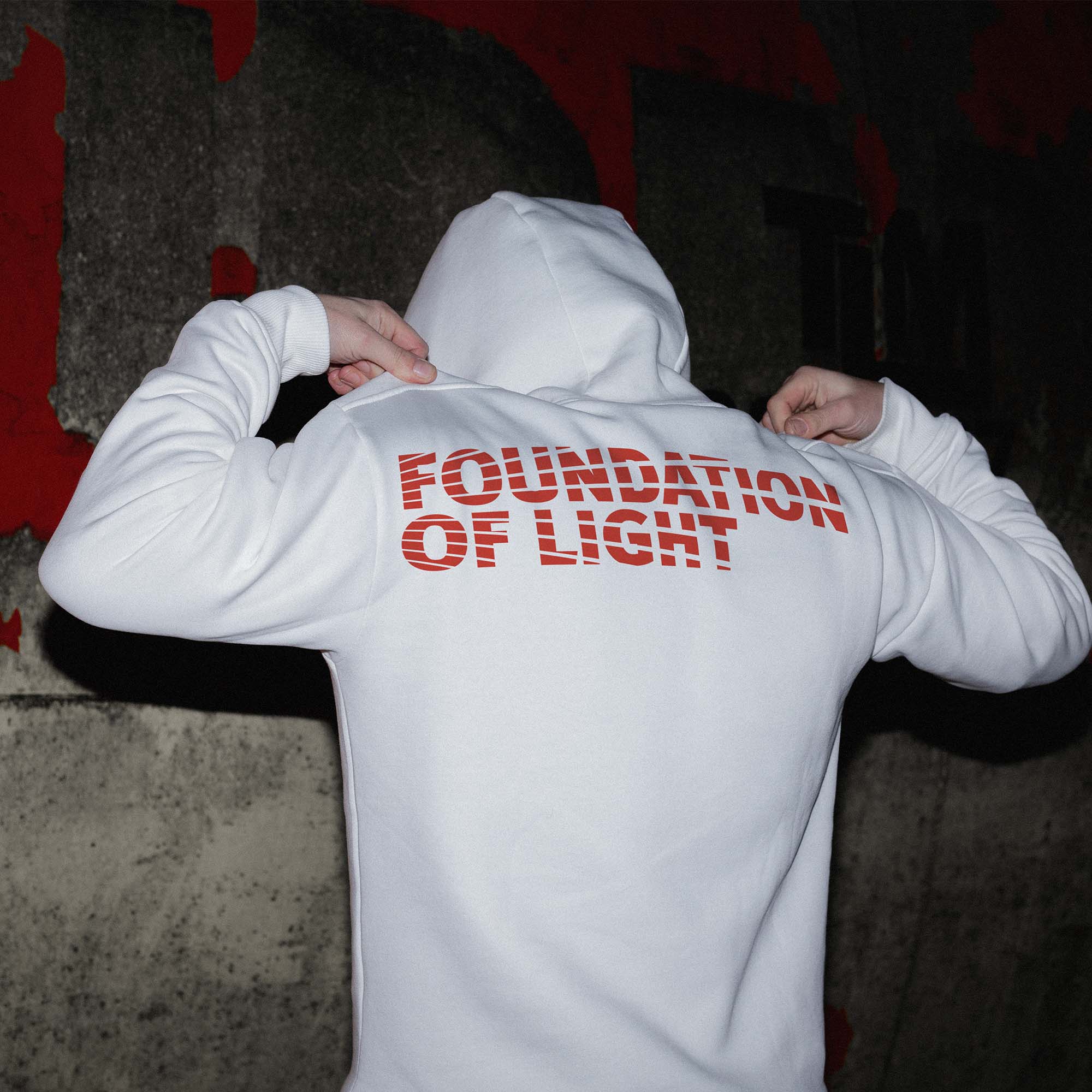 Back of a young person wearing a white hoodie with the Foundation of Light logo across the shoulders.