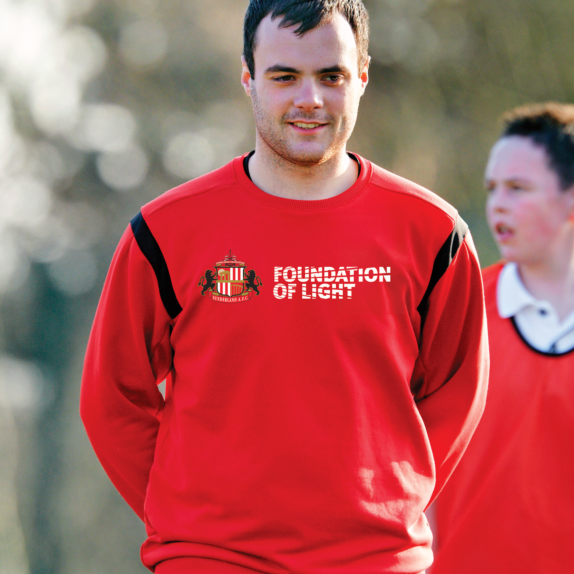 Image of Foundation of Light coach working outside on a training field with school children. His sweatshirt has the Foundation of Light logo across the chest.