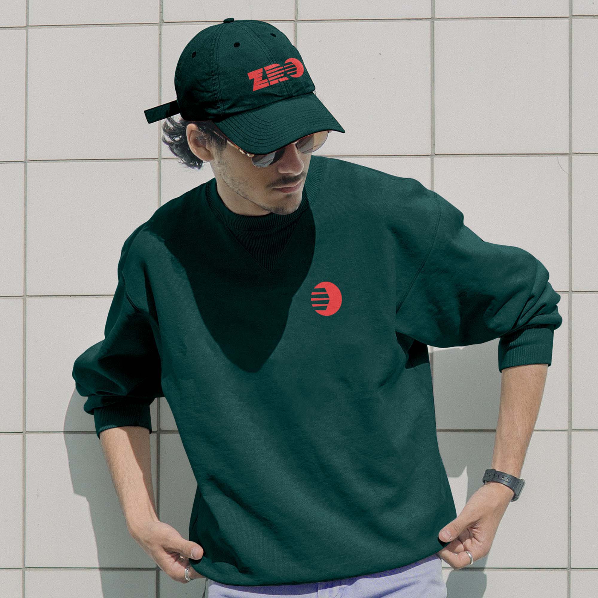 ZRO branded cap and sweat shirt being worn by a young man stood against a white tiled wall.