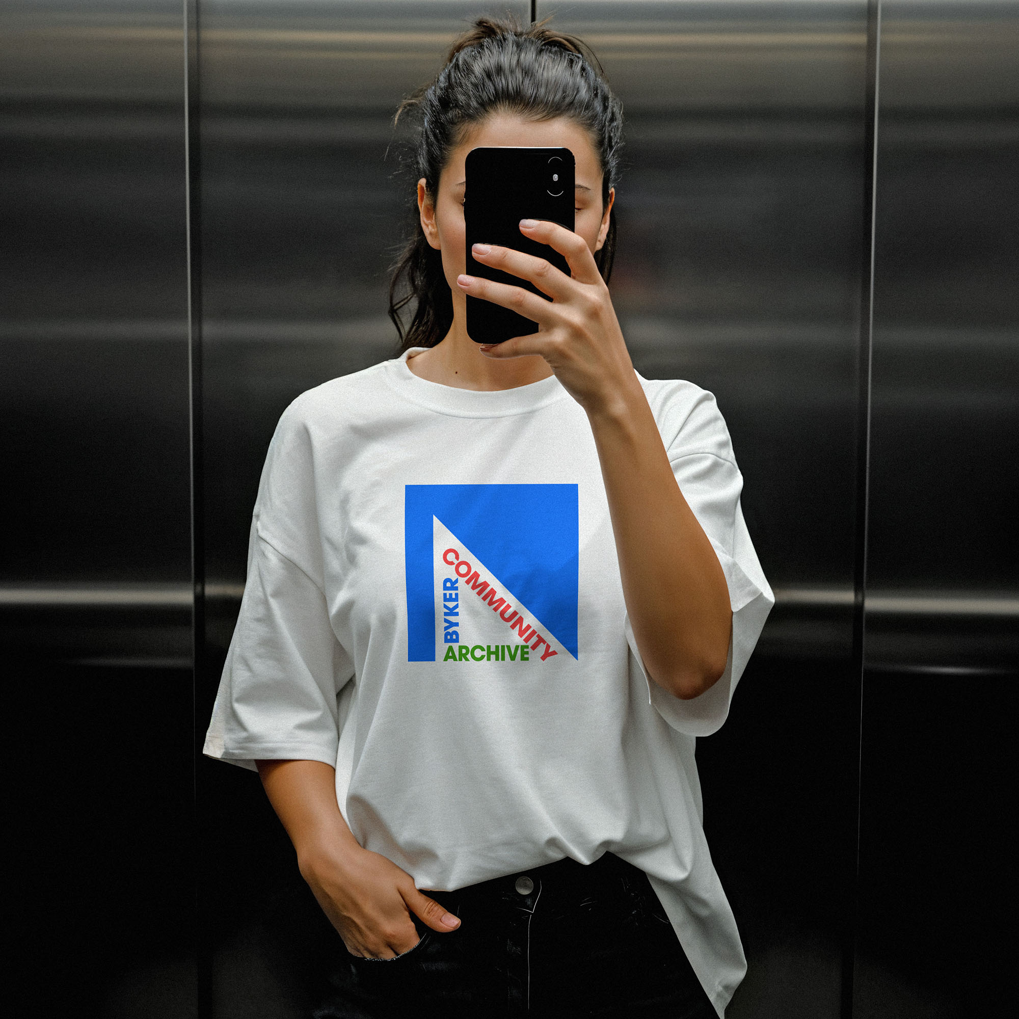 Byker Community Archive branded T-shirt worn by young woman in a elevator.