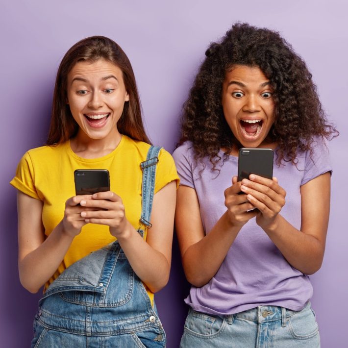 Two women grinning excitedly at their phones